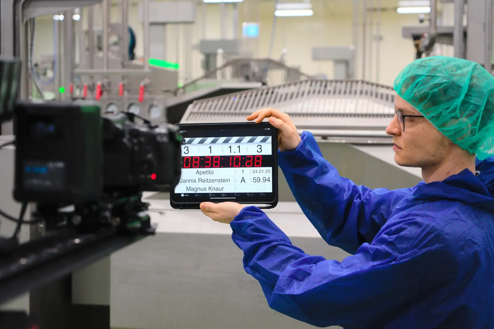A team member in protective clothing holds a digital clapperboard labeled Apetito in front of the camera