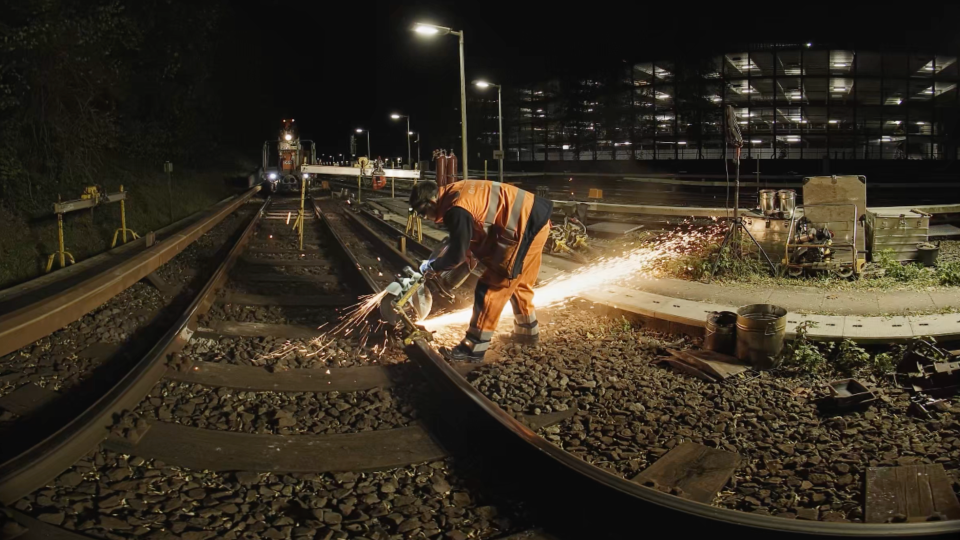 At night, a track worker cuts a rail with an abrasive cut-off saw, sending sparks flying