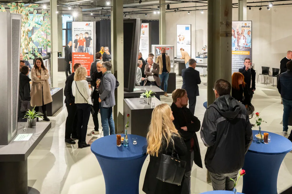 Guests at the opening of the Arbeitswelten in a hall with high tables, exhibits, and company displays