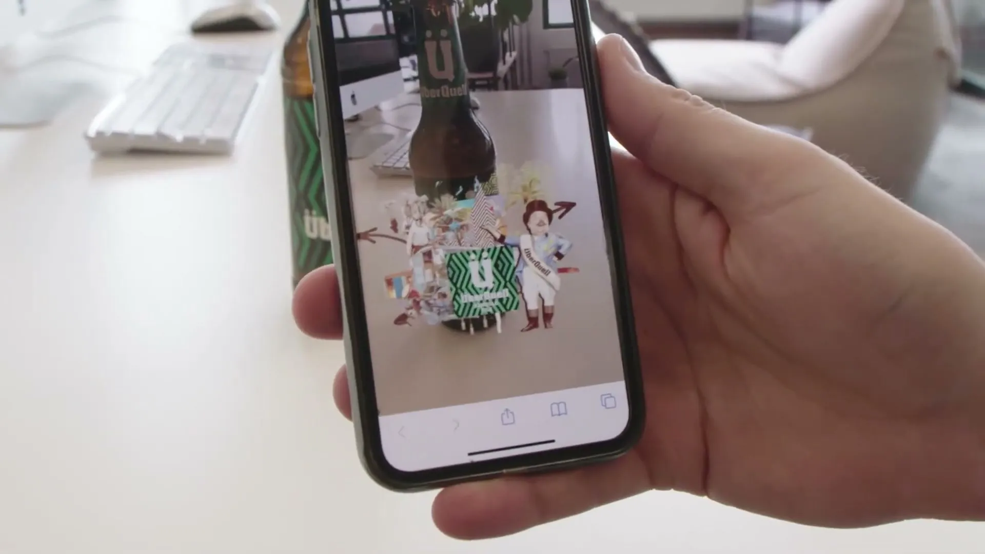 Auf dem Smartphone entfaltet sich am Etikett der Bierflasche eine bunte Collage, daneben steht Zirkusdirektor Johnny