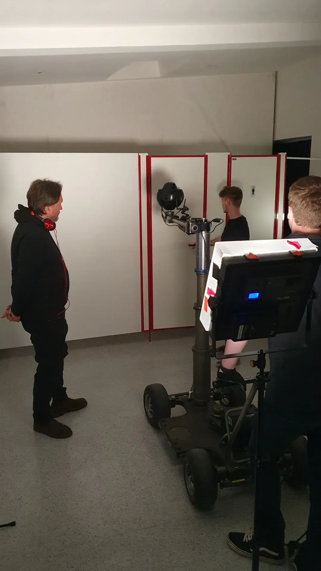 Probe einer Kamerafahrt: 360°-Kamera an einem Kamerawagen vor Toilettenkabinen, daneben ein Darsteller und zwei Crewmitglieder