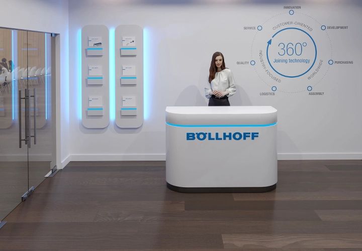 Reception desk with the Böllhoff logo and a woman behind it, with a graphic on the wall reading 360° Joining technology
