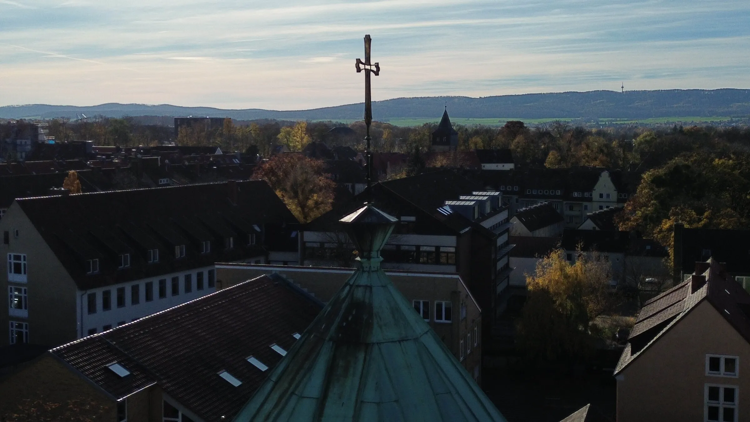 Drohnenaufnahme: Das Turmkreuz der Kirche Zum Heiligen Kreuz vor den Dächern von Hildesheim und den Hügeln am Horizont