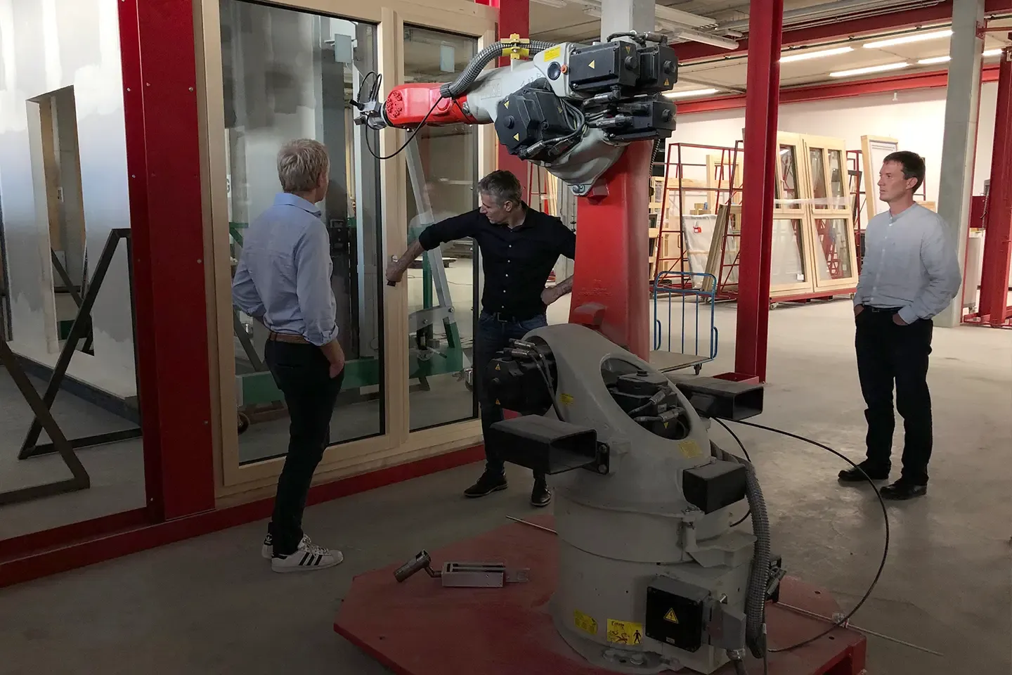 Three men at a test rig with an industrial robot and a window unit in a hall
