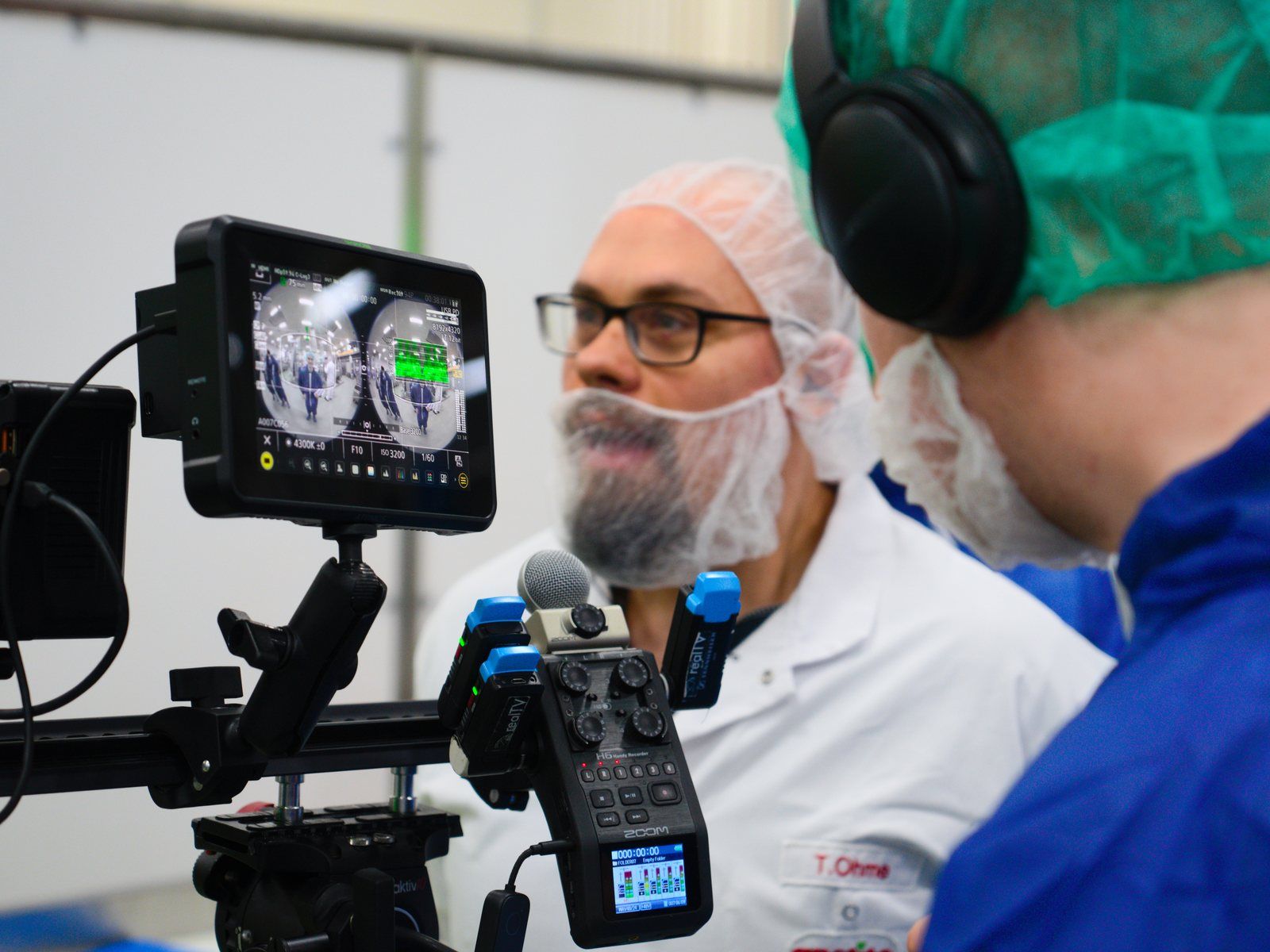 Camera with preview monitor, next to it two people in hygiene clothing during an interview