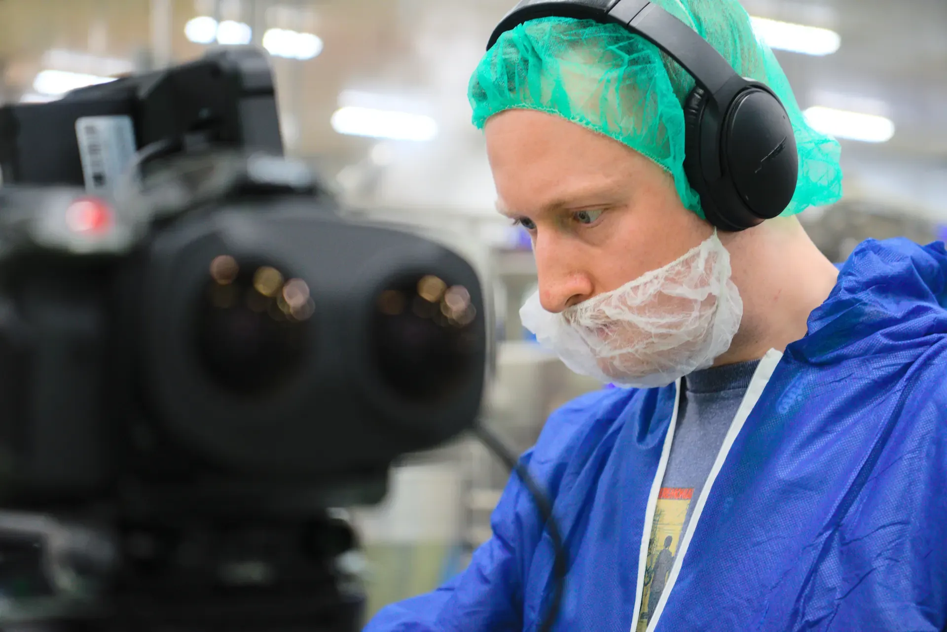 A camera operator wearing a hairnet, beard cover, and headphones works on the 3D camera