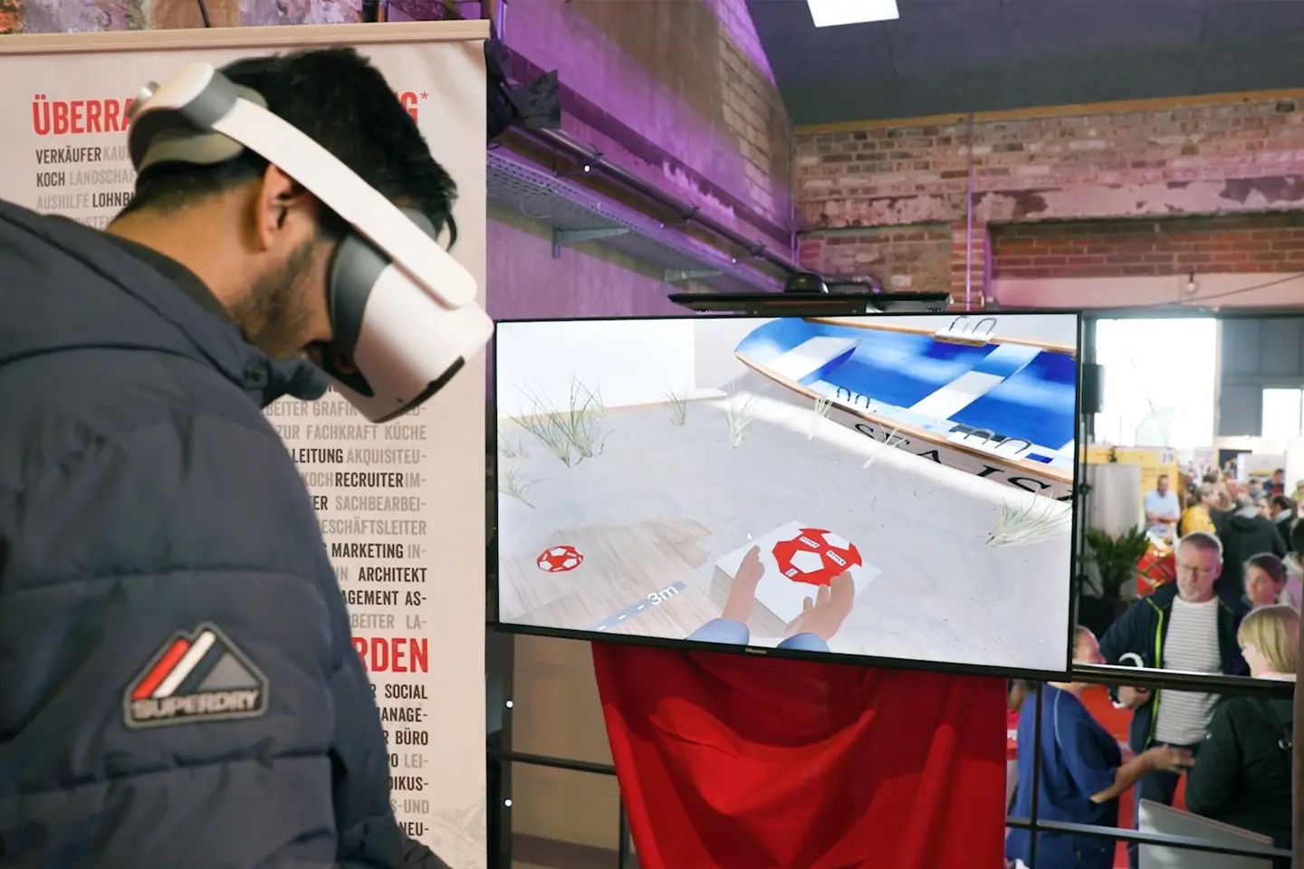 A young man wearing a VR headset at the Kaufhaus STOLZ booth, next to a screen showing what he sees in the headset