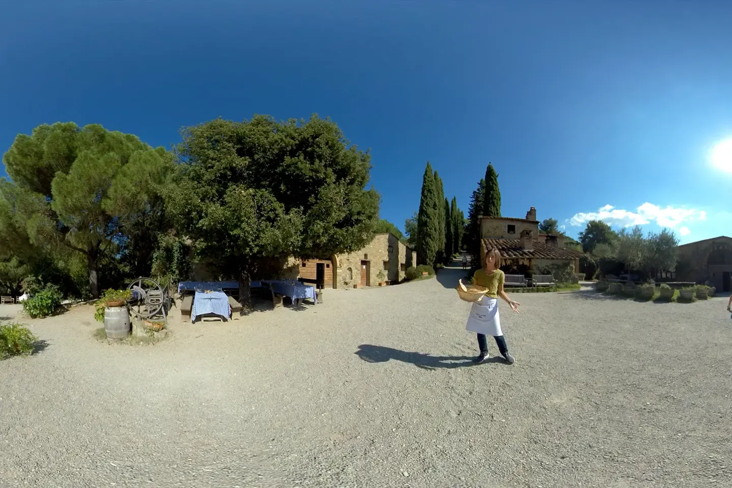 360° shot of the Fattoria courtyard with stone houses, cypress trees, and a staff member holding a bread basket