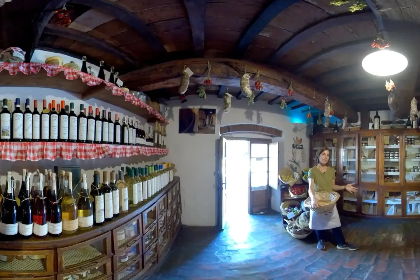360° shot of the farm store with wine shelves, hanging sausages, and a staff member holding a bread basket