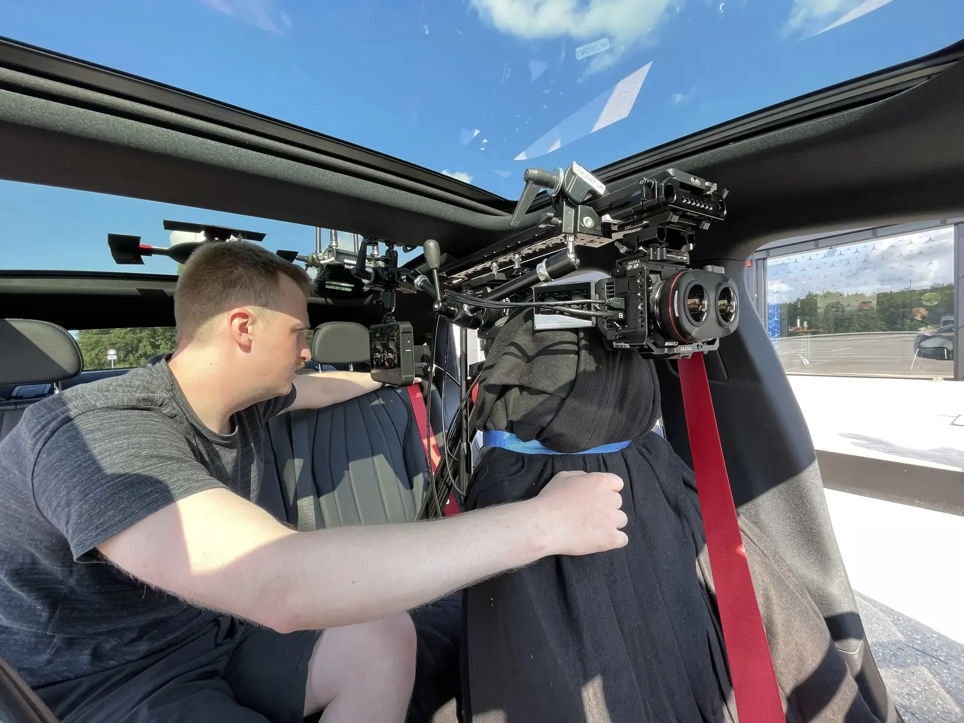 A technician sets up a 3D camera in a car, mounted on a bracket above the driver’s seat