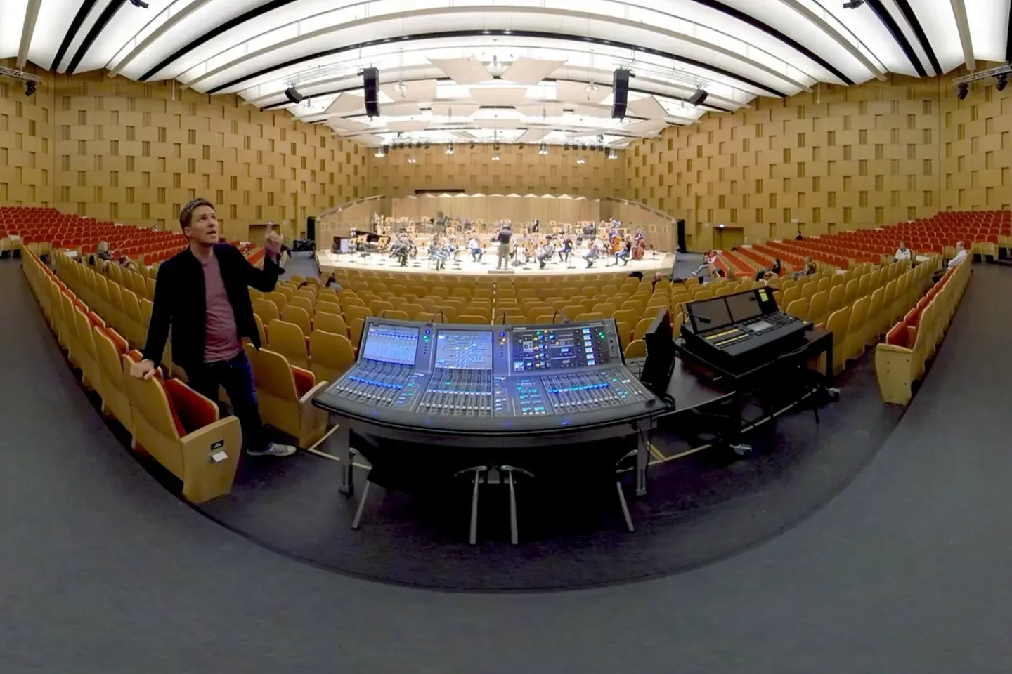360° shot of a concert hall with an orchestra rehearsing, a mixing desk in front and the host between the rows of seats