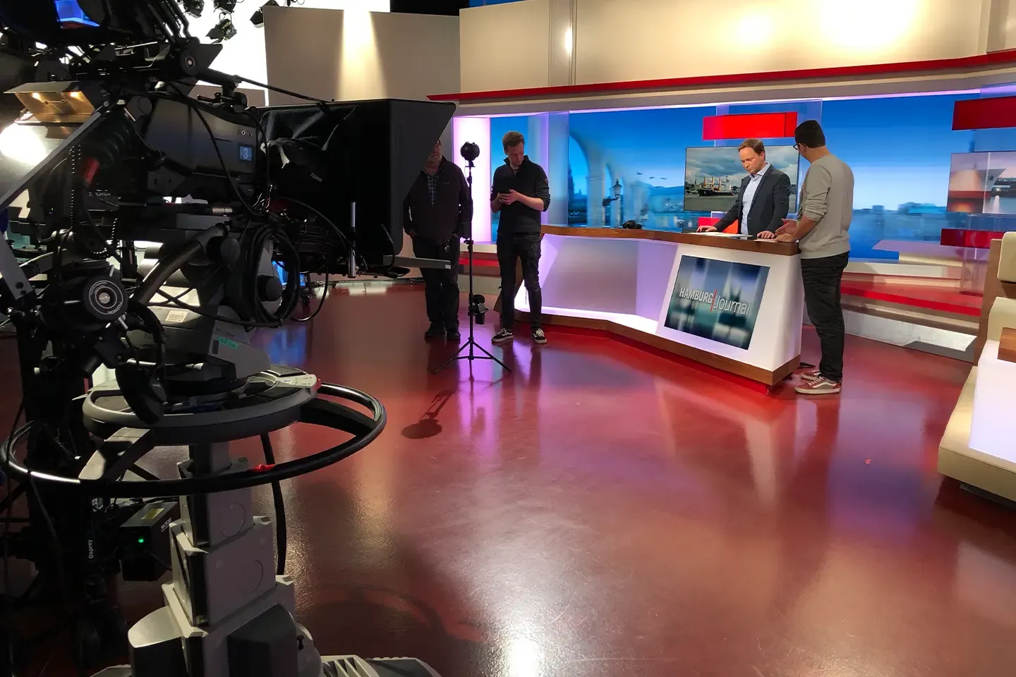 Filming in the Hamburg Journal studio: 360° camera on a tripod, the host at the desk, a studio camera on the left