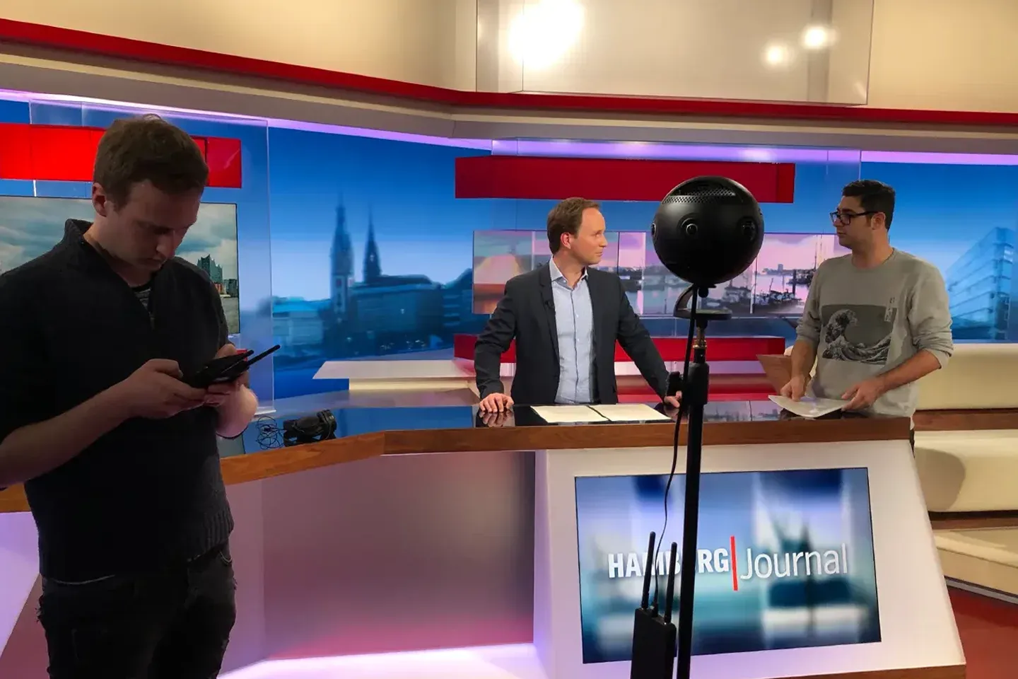 360° camera in the Hamburg Journal studio, behind it the host at the desk and two members of the film crew