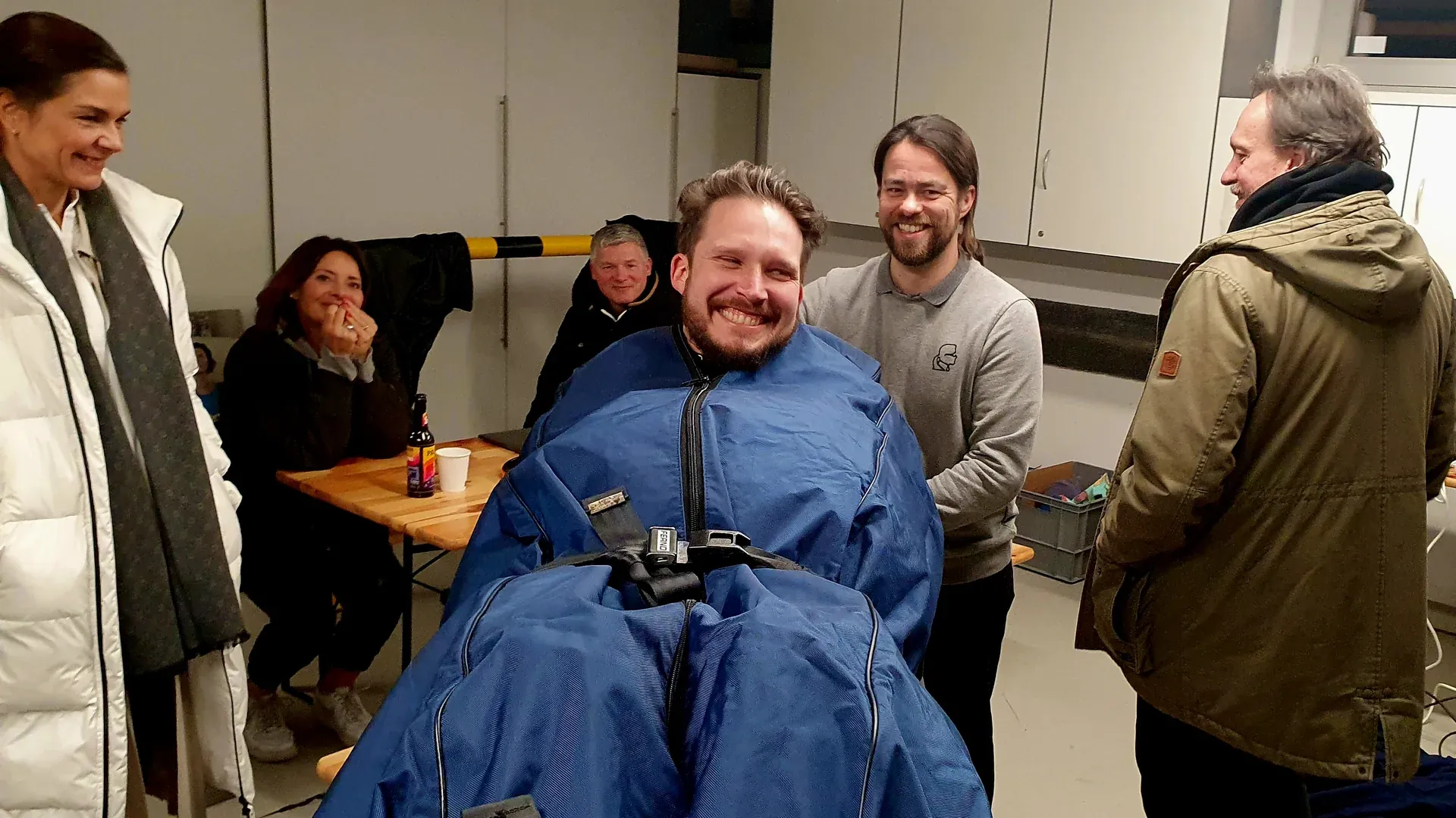 Ein Mann steckt lachend im Leichensack auf einer Trage, umringt von gut gelaunten Crewmitgliedern und Darstellern