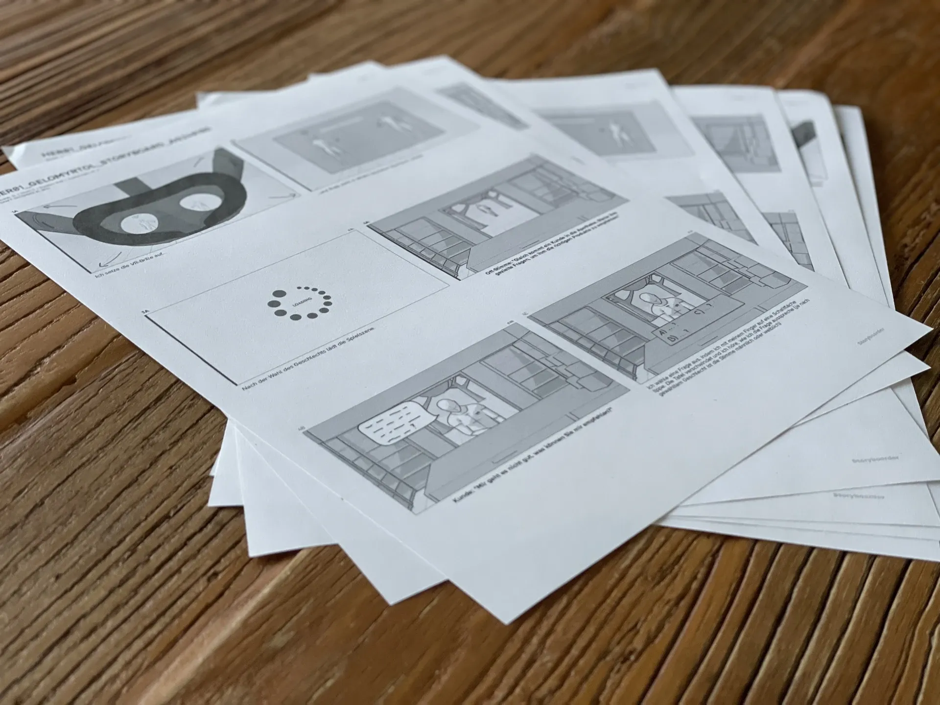 Printed storyboard pages with sketches of a VR application fanned out on a wooden table