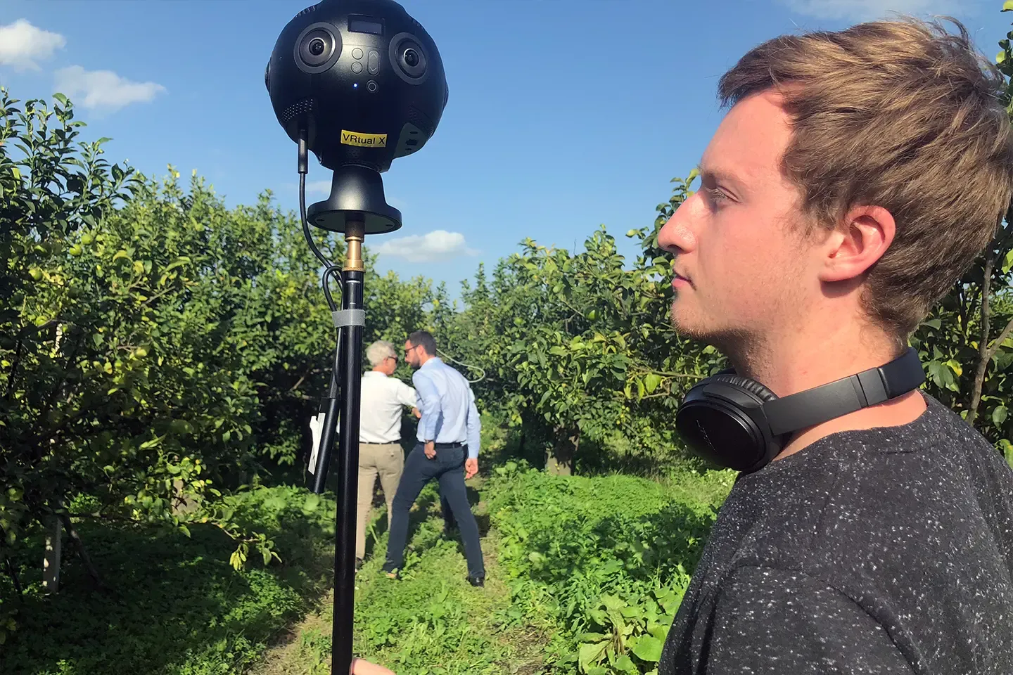 360° camera with a VRtual X sticker in a citrus plantation, a camera operator wearing headphones on the right
