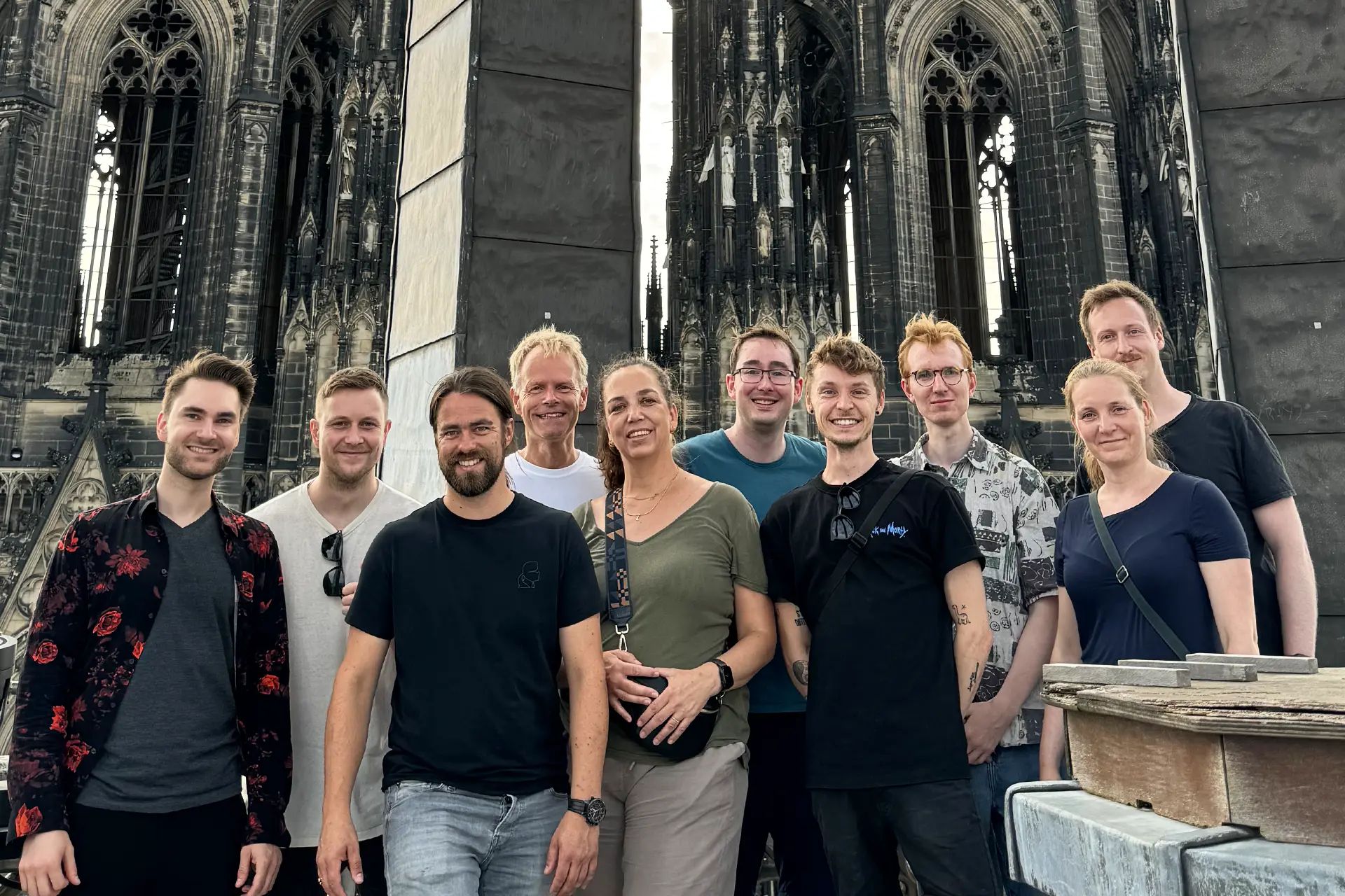 Zehn Mitarbeiterinnen und Mitarbeiter von VRtual X stehen gemeinsam auf einem Baugerüst vor einer gotischen Kirche